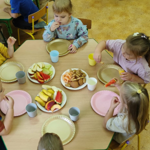 Dzieci siedzą przy stoliku i jedzą przekąski