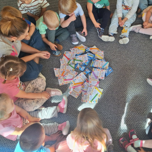 Dzieci siedzą na dywanie w kole. W środku leżą upominki.