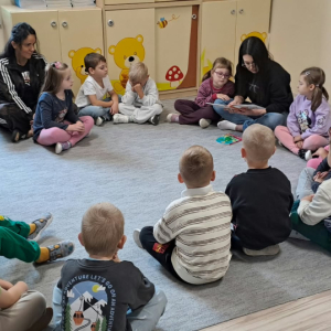 Dzieci siedzą na dywanie. Pani czyta książkę