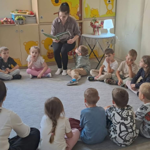 Dzieci siedzą na dywanie. Pani czyta książkę