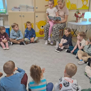 Dzieci siedzą na dywanie. Pani czyta książkę