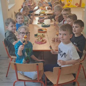Dzieci siedzą przy stoliku i robią szaszłyki z owoców