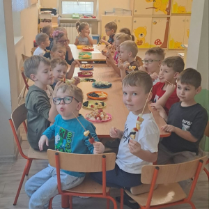Dzieci siedzą przy stoliku i robią szaszłyki z owoców