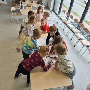 Dzieci stoją przy stoliku i wykonują prace plastyczną