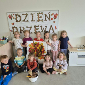Dzieci pozują do zdjęcia , trzymają prace zbiorową wykonaną naturalnymi lisćmi.
