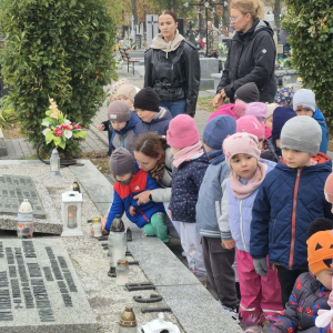 Dzieci stawiają zapalone znicze na pomniku